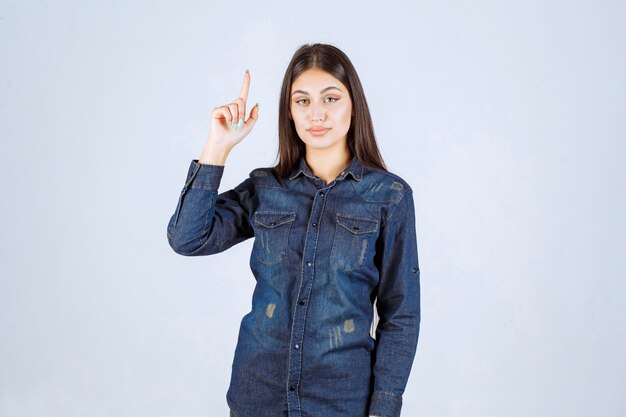 Giovane donna in camicia di jeans che punta a qualcosa al rialzo