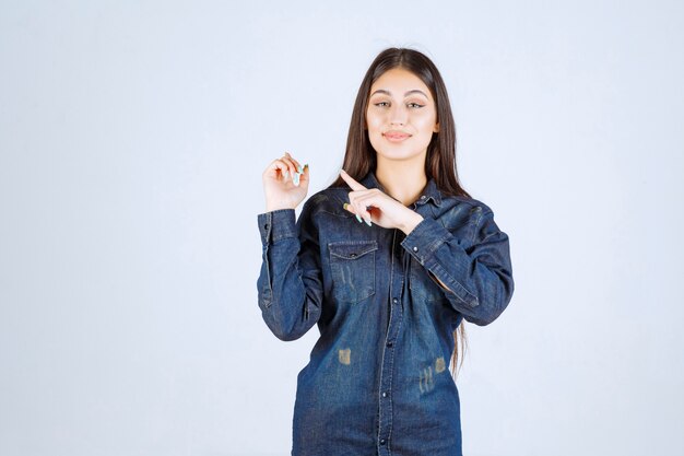 Giovane donna in camicia di jeans che punta a qualcosa dietro