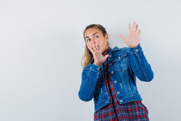 Giovane donna in camicia, giacca alzando le mani per difendersi e guardando spaventato, vista frontale.