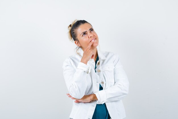 Giovane donna in camicia, giacca bianca con il dito sulla bocca e sguardo pensieroso, vista frontale.