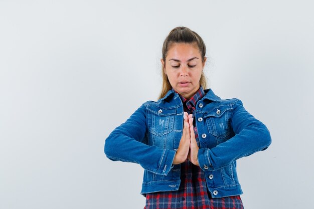 Giovane donna in camicia, giacca che mostra il gesto di namaste e che sembra concentrata, vista frontale.