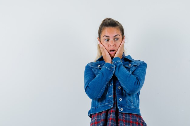 Giovane donna in camicia, giacca con le mani sulle guance e guardando sorpreso, vista frontale.