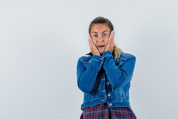 Giovane donna in camicia, giacca tenendo le mani sulle guance e guardando felice, vista frontale.