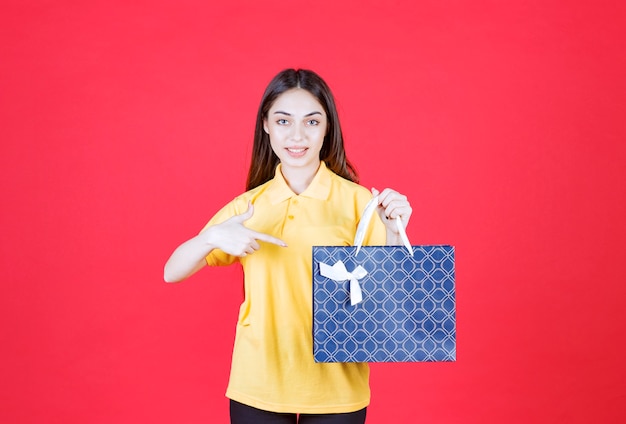 Giovane donna in camicia gialla che tiene una borsa della spesa blu