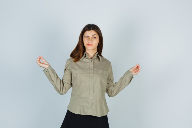 Giovane donna in camicia, gonna che mostra gesto di meditazione e sembra rilassata