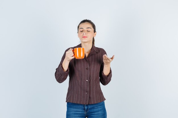 Giovane donna in camicia, jeans che odorano l'aroma del tè e sembrano contenti, vista frontale.