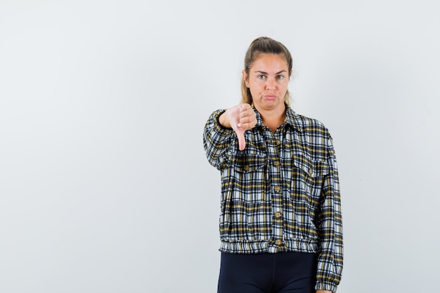 Giovane donna in camicia, pantaloncini che mostra il pollice verso il basso e sembra sicura di sé, vista frontale.