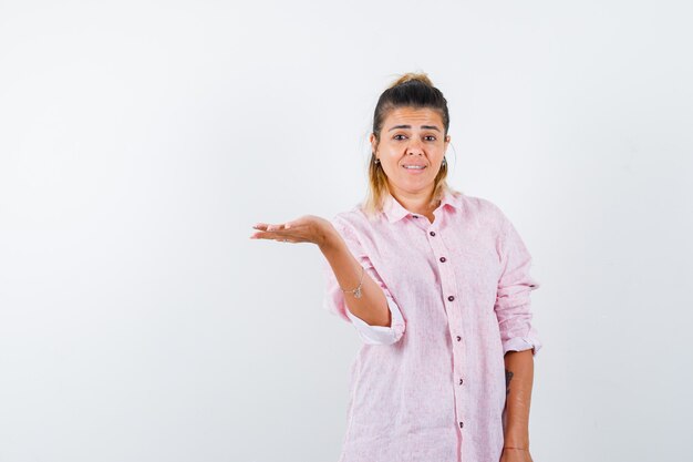 Giovane donna in camicia rosa che finge di tenere o mostrare qualcosa e sembra gentile