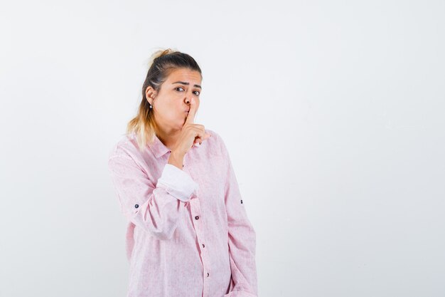 Giovane donna in camicia rosa che mostra gesto di silenzio e sembra ragionevole