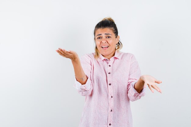 Giovane donna in camicia rosa che mostra gesto impotente e che sembra confusa