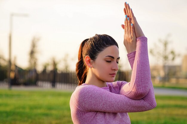 giovane donna in camicia rosa e pantaloni seduto sull'erba all'interno del parco meditando e facendo yoga in diverse pose