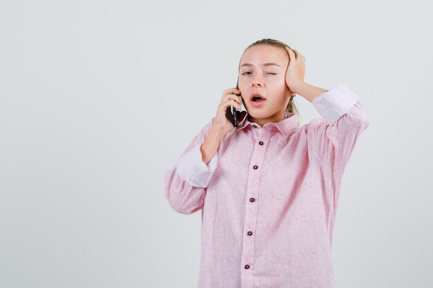 Giovane donna in camicia rosa, parlando al telefono cellulare e ammiccante