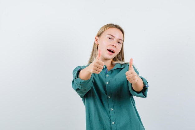 Giovane donna in camicia verde che mostra il doppio pollice in alto e sembra sicura