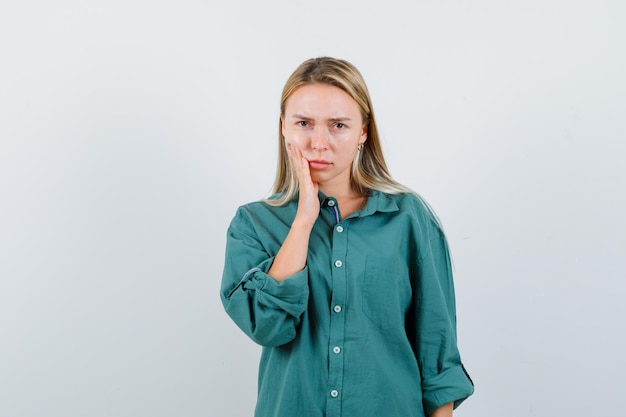 Giovane donna in camicia verde che tiene la mano sulla guancia e sembra sconvolta