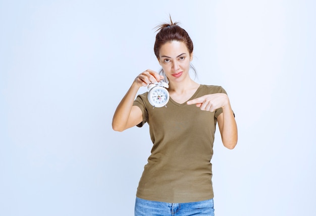 Giovane donna in camicia verde con in mano una sveglia