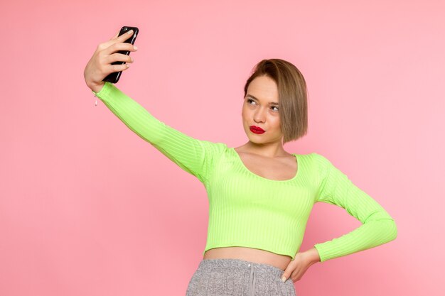 giovane donna in camicia verde e pantaloni grigi prendendo un selfie