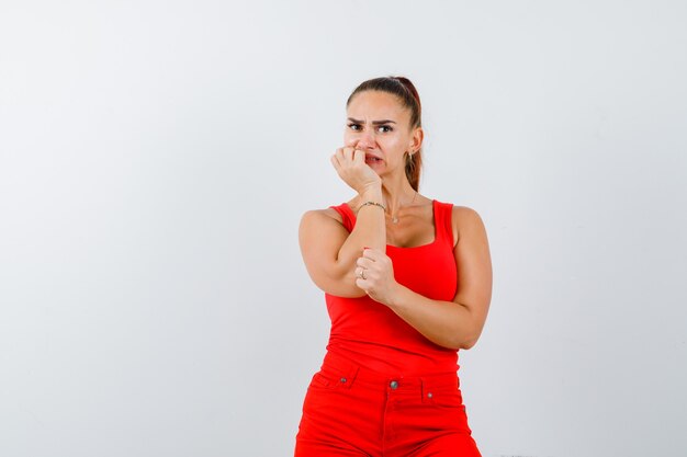 Giovane donna in canottiera rossa, pantaloni rossi appoggiando il mento sulle mani e guardando ansioso, vista frontale.