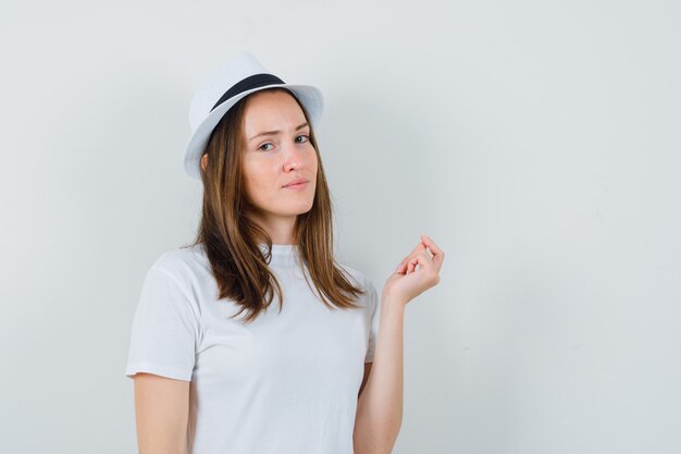 Giovane donna in cappello bianco della maglietta che guarda l'obbiettivo mentre pensa e sembra ragionevole