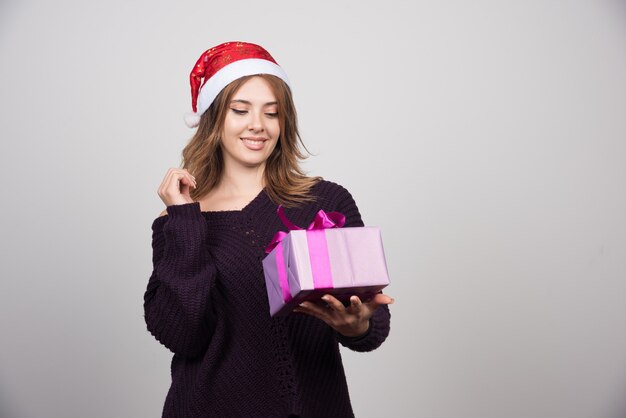 Giovane donna in cappello della Santa che esamina un regalo del contenitore di regalo.