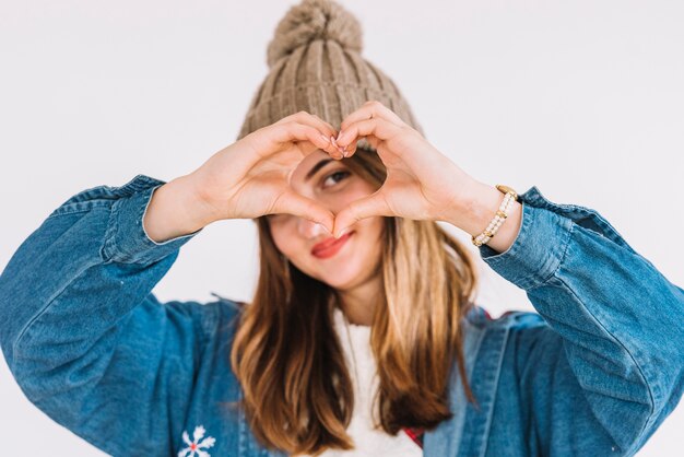 Giovane donna in cappello di bobble che mostra simbolo del cuore