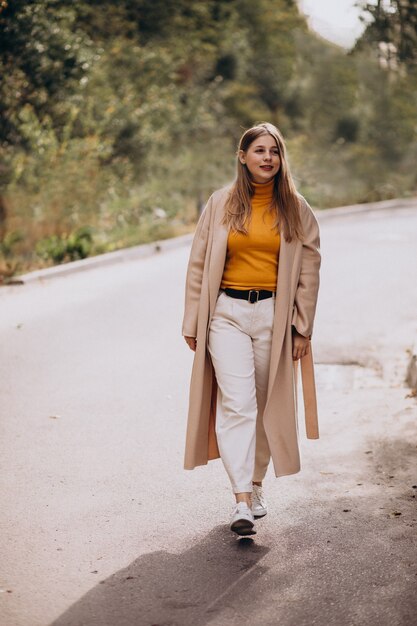 Giovane donna in cappotto beige che cammina nel parco