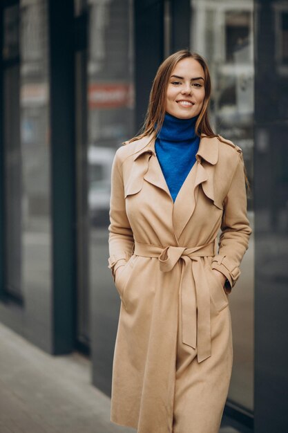 Giovane donna in cappotto beige che cammina per strada