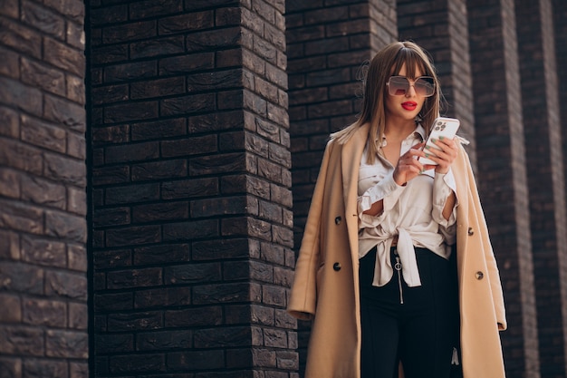 Giovane donna in cappotto beige usando il telefono in strada