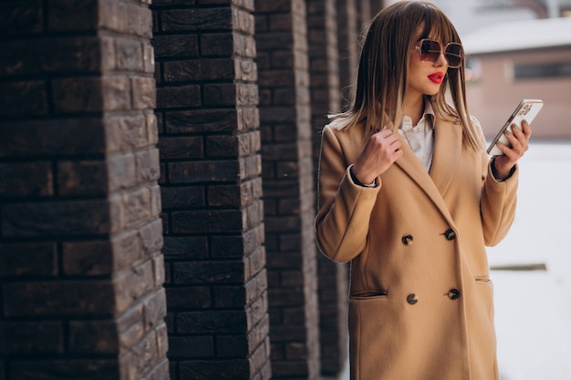 Giovane donna in cappotto beige usando il telefono in strada