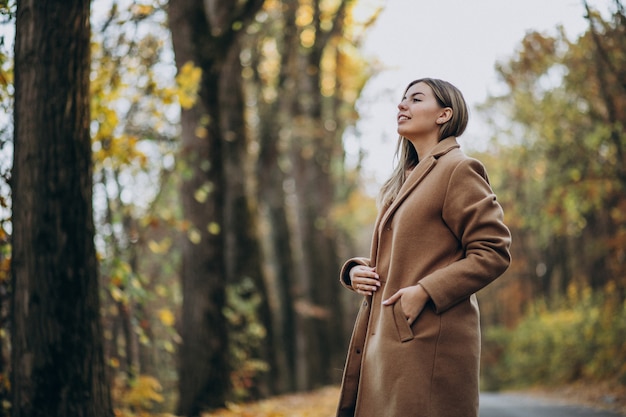 Giovane donna in cappotto che sta sulla strada in un parco di autunno