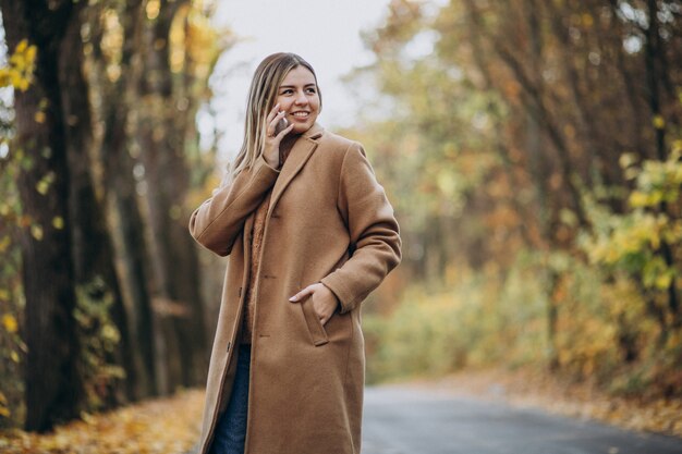 Giovane donna in cappotto che sta sulla strada in un parco di autunno