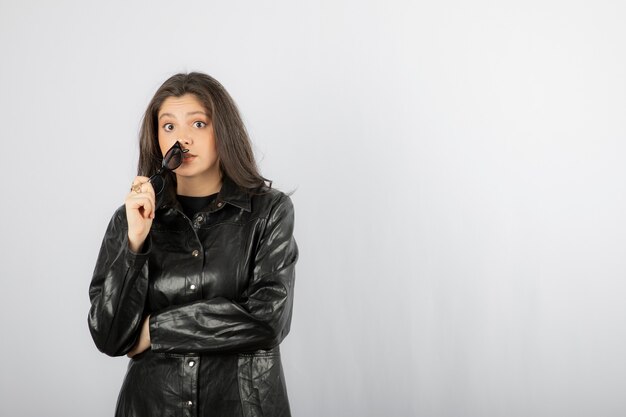 giovane donna in cappotto nero che tiene gli occhiali e posa.