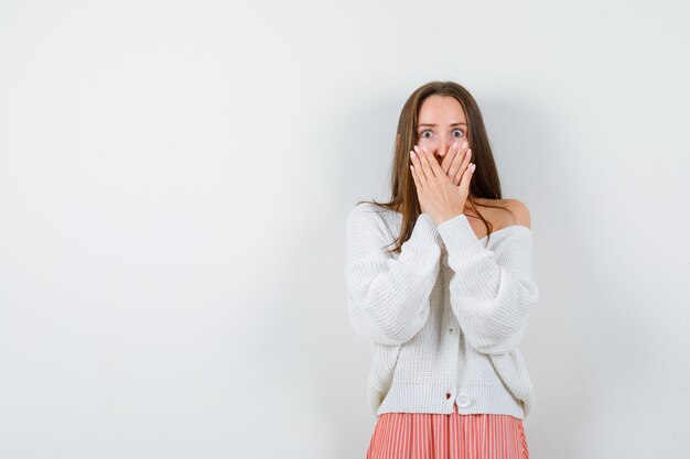 Giovane donna in cardigan e gonna mantenendo le mani sulla bocca cercando paura isolata