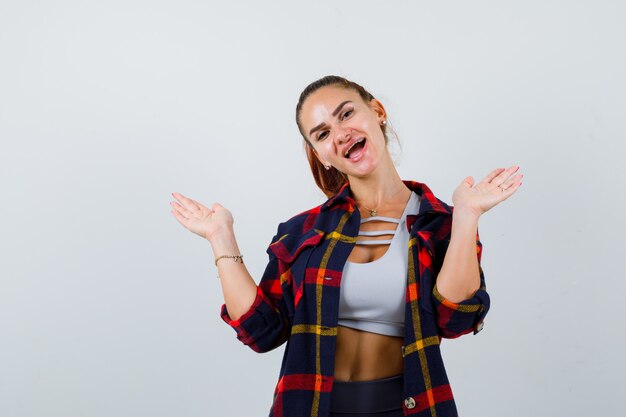 Giovane donna in crop top, camicia a scacchi, pantaloni allarga i palmi e sembra allegra, vista frontale.