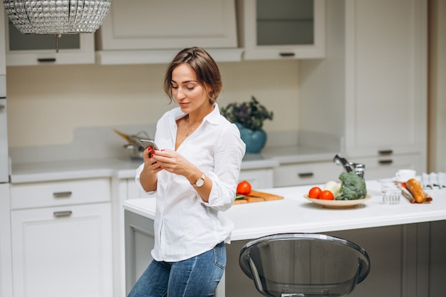 Giovane donna in cucina cucinare la colazione e parlare al telefono