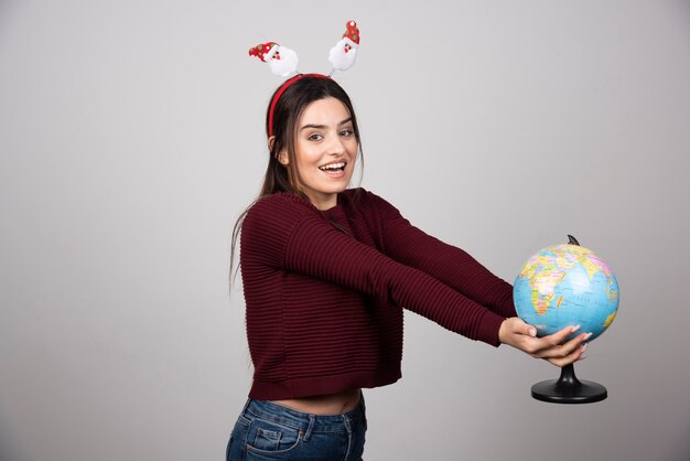 Giovane donna in fascia di Natale in possesso di un globo terrestre.