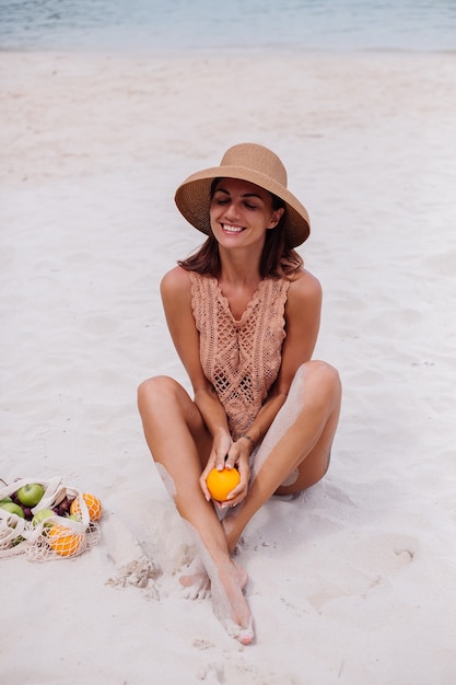 Giovane donna in forma abbronzata abbastanza caucasica in vestiti a maglia e cappello sulla spiaggia