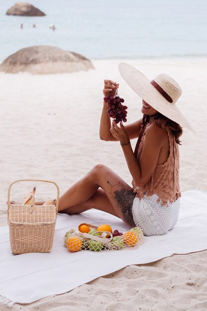 Giovane donna in forma abbronzata abbastanza caucasica in vestiti a maglia e cappello sulla spiaggia