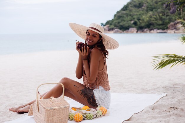 Giovane donna in forma abbronzata abbastanza caucasica in vestiti a maglia e cappello sulla spiaggia