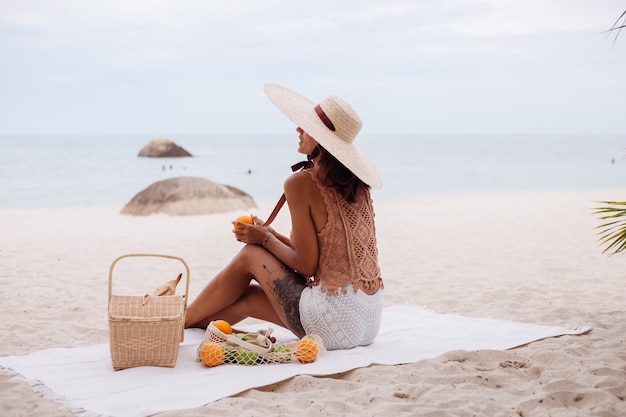 Giovane donna in forma abbronzata abbastanza caucasica in vestiti a maglia e cappello sulla spiaggia