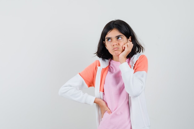 Giovane donna in giacca, camicia rosa che tiene la mano sul mento e sembra nervosa