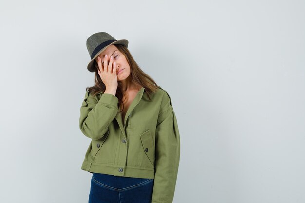 Giovane donna in giacca pantaloni cappello tenendo la mano sul viso e guardando esausto