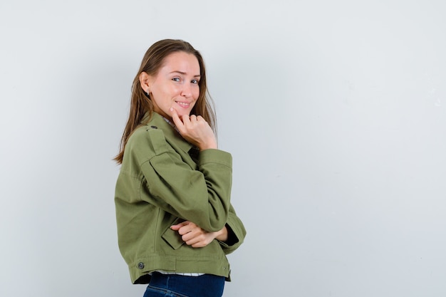 Giovane donna in giacca verde in piedi in posa di pensiero e dall'aspetto elegante.