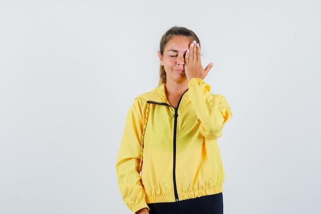 Giovane donna in impermeabile giallo che copre l'occhio sinistro con la mano