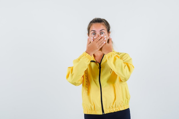 Giovane donna in impermeabile giallo che tiene le mani sulla bocca e che sembra spaventata