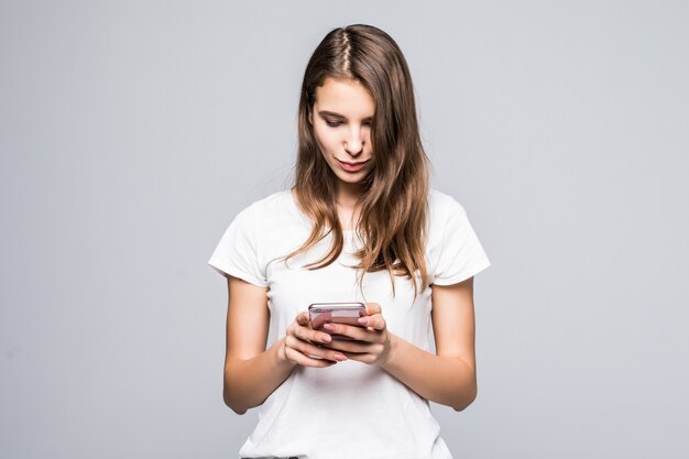 Giovane donna in maglietta bianca e blue jeans stare con il telefono davanti a sfondo bianco studio