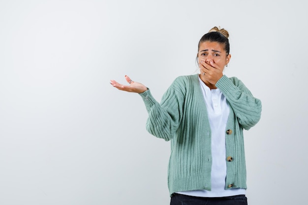 Giovane donna in maglietta bianca e cardigan verde menta che pizzica il naso a causa del cattivo odore e sembra infastidita