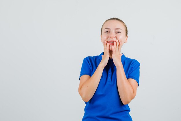 Giovane donna in maglietta blu che tiene le mani vicino alla bocca e che sembra felice