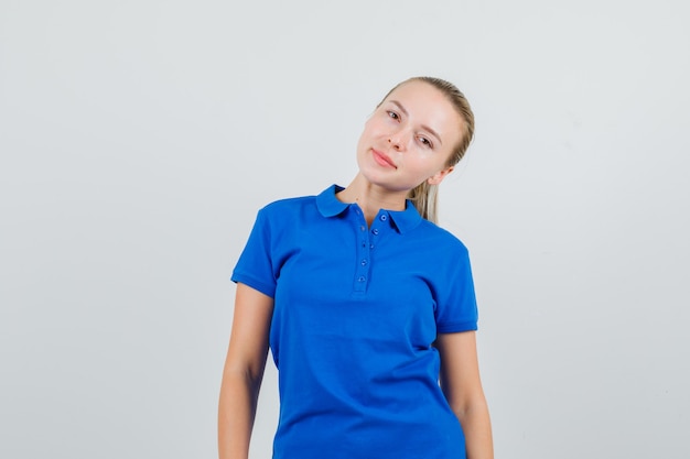 Giovane donna in maglietta blu chinando la testa sulla spalla e guardando carino