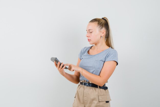 Giovane donna in maglietta e pantaloni utilizzando la calcolatrice e guardando occupato