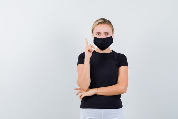 Giovane donna in maglietta nera, maschera rivolta verso l'alto e guardando triste, vista frontale.